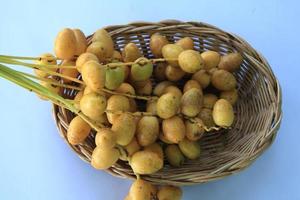 tâmaras amarelas maduras são cultivadas organicamente, doces e deliciosas e frescas em uma cesta de tecido em um fundo azul e branco com as mãos de um homem segurando-as. foto