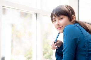 bela jovem escritora asiática sorrindo pensando a ideia e escrevendo no caderno ou diário com feliz, estilo de vida da garota asiática é estudante, planejamento feminino de trabalho, educação e conceito de negócios. foto