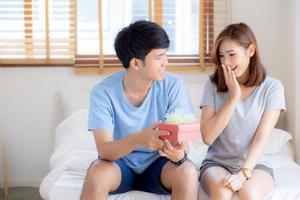 lindo jovem casal asiático apaixonado caixa de presente surpresa no quarto em casa, aniversário de família com desfrutar e romântico juntos esposa e marido com relacionamento, celebrando o conceito de dia dos namorados. foto