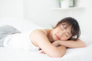bela jovem asiática sorri dormindo deitada na cama com lazer confortável e feliz no quarto, beleza ásia menina bem-estar com relaxar e fresco para o conceito de saúde. foto