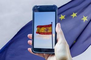 bandeira da espanha em uma tela de smartphone na frente de uma bandeira da união europeia. foto