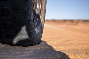 close-up de rodas de carro offroad e pneu achatado estacionado na areia foto