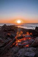 fogueira com queima de lenha durante o belo pôr do sol na praia foto