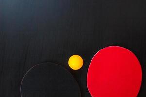 duas raquetes de tênis de mesa ou ping pong e bola em um fundo preto foto