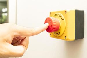 botão de parada e a mão do trabalhador prestes a pressioná-lo. botão de parada de emergência. grande botão de emergência vermelho ou botão de parada para pressão manual. foto