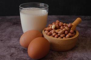 grupo alimentar proteico. amendoim cru na tigela de madeira, ovo de galinha e um copo de leite no fundo de cimento. comida saudável. foto