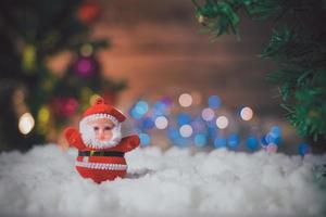 boneca de papai noel colocada na neve e o fundo da árvore de natal com bokeh e madeira. foto
