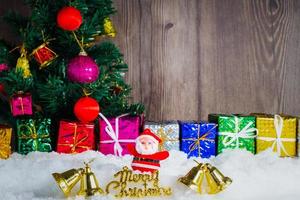 boneca de papai noel e decorações colocadas na neve e no fundo e na madeira da árvore de natal. foto