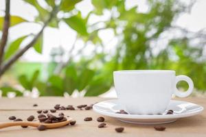 uma xícara de café branco com um pires e uma colher é colocada em uma placa de madeira no fundo da natureza da paisagem. foto