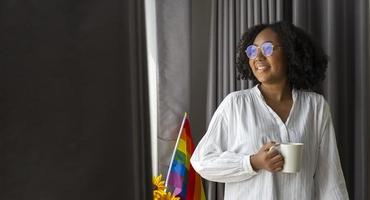 garota afro-americana segurando a bandeira do arco-íris lgbtq em seu quarto para sair do armário e celebração do mês do orgulho para promover a diversidade sexual e igualdade no conceito de orientação homossexual foto