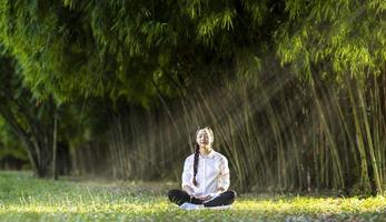 mulher praticando relaxantemente meditação na floresta de bambu para alcançar a felicidade da sabedoria da paz interior para a mente de bem-estar saudável e o conceito de alma de bem-estar foto