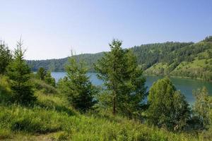 lago pitoresco cercado por montanhas com grama verde e árvores. foto