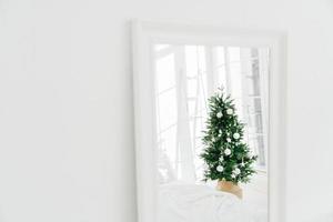árvore de natal decorada refletindo no espelho, quarto espaçoso branco. quarto com decoração de ano novo. estilo clássico moderno. véspera de natal em casa foto