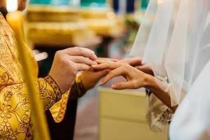 padre coloca o anel no dedo da noiva durante a cerimônia de casamento na igreja. troca de anéis. vista horizontal. conceito de casamento foto