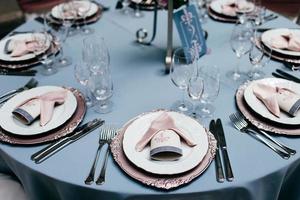 compromissos de mesa. configuração de mesa com pratos vazios, garfos, copos e facas e toalhas de mesa azul claro. mesa servida no restaurante para ocasiões especiais. conjunto de café ou restaurante.
