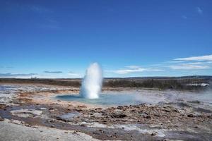 erupção do gêiser strokkur no meio da paisagem contra o céu azul durante o dia ensolarado foto