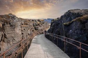 turistas andando na ponte entre formações rochosas no parque nacional thingvellir foto