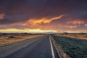 estrada vazia em meio a paisagem vulcânica contra céu dramático durante o pôr do sol foto