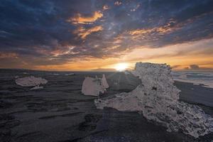 close-up do pedaço de iceberg na areia preta da praia de diamante contra o céu ao pôr do sol foto