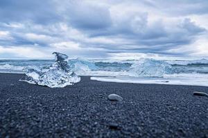 pedaços de iceberg na praia de areia preta com ondas correndo na costa contra o céu foto