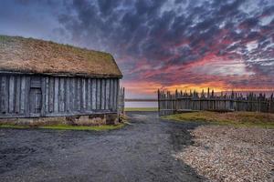 casa tradicional de madeira cercada por cerca contra o céu dramático durante o pôr do sol foto