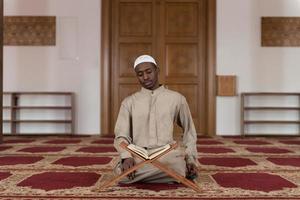 homem muçulmano em dishdasha está lendo o Alcorão foto