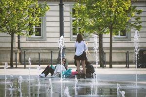 Vilnius, Lituânia. 06 de junho de 2022 - alunas adolescentes sentadas na calçada se divertindo perto da fonte na praça da cidade em frente à academia de música foto