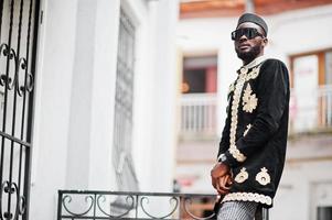 mega homem africano elegante em pose de jaqueta tradicional. elegante negro de chapéu e óculos de sol com charuto na mão. foto