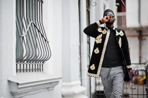 mega homem africano elegante em pose de jaqueta tradicional. elegante negro de chapéu e óculos de sol com charuto na mão. foto