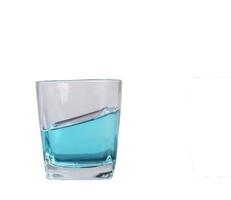 copo para licor colocar líquido azul feito de vidro descansando sobre uma mesa inclinada fundo branco foto