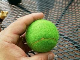 mão segurando uma bola de tênis verde sobre mesa de metal foto