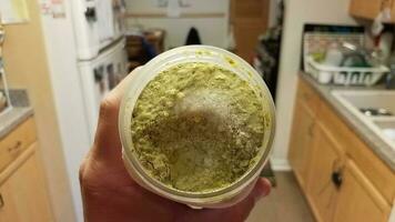 mão segurando o recipiente de molho pesto verde com gelo na cozinha foto