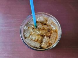 refrigerante e gelo em um copo com um canudo azul na mesa foto