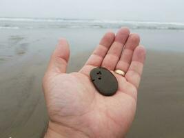 mão com anel de ouro segurando pedra com buracos na praia foto