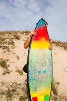 jovem surfista na praia se esconde atrás de sua prancha de surf colorida foto