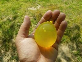 mão segurando balão de água amarelo sobre grama verde foto