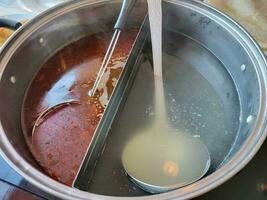 panela quente chinesa com caldo e colheres picantes e regulares foto