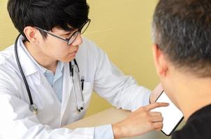 jovem médico asiático explicando com paciente do sexo masculino sobre tablet digital no escritório foto