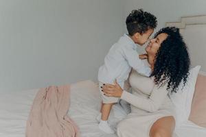 mãe grávida feliz abraçando adorável filho enquanto está sentado na cama foto