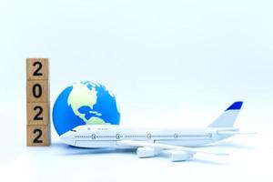 2022 ano novo e conceito de viagens. closeup do modelo de brinquedo de avião com mini bola mundial com pilha de bloco de número de madeira sobre fundo branco. foto