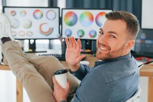 sentado na cadeira, relaxado. designer masculino trabalhando no escritório usando pc foto