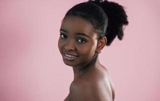 olhando na câmera. retrato de jovem afro-americana que é contra o fundo rosa foto