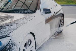 carro sujo preto em espuma de sabão branco na estação de serviço de lavagem de carros foto