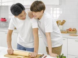 jovem casal lgbt masculino asiático feliz olhando contato visual juntos durante o cozimento da salada de pão na cozinha branca com um sorriso no rosto. foco seletivo. foto