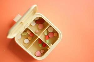 close-up de pílulas médicas em uma caixa de pílulas em fundo laranja foto
