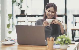 mão feminina trabalhando com tablet digital e segurando a xícara de café no espaço de trabalho criativo escuro. foto