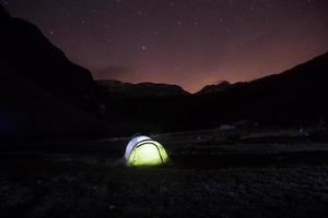 tenda de pé em um pasto de montanha sob o céu estrelado