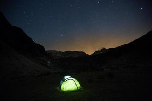tenda de pé em um pasto de montanha sob o céu estrelado