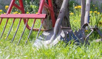 ferramentas de jardinagem. ferramentas de jardim no fundo de um jardim na grama verde. ferramenta de trabalho de verão. pá, garfo e fermento em pó empilhados no jardim lá fora. o conceito de ferramentas de jardinagem. foto