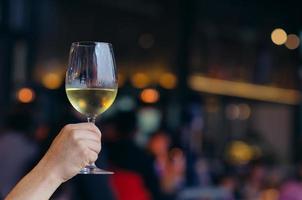 mão segurando um copo de vinho branco com luz colorida bokeh no restaurante. foto